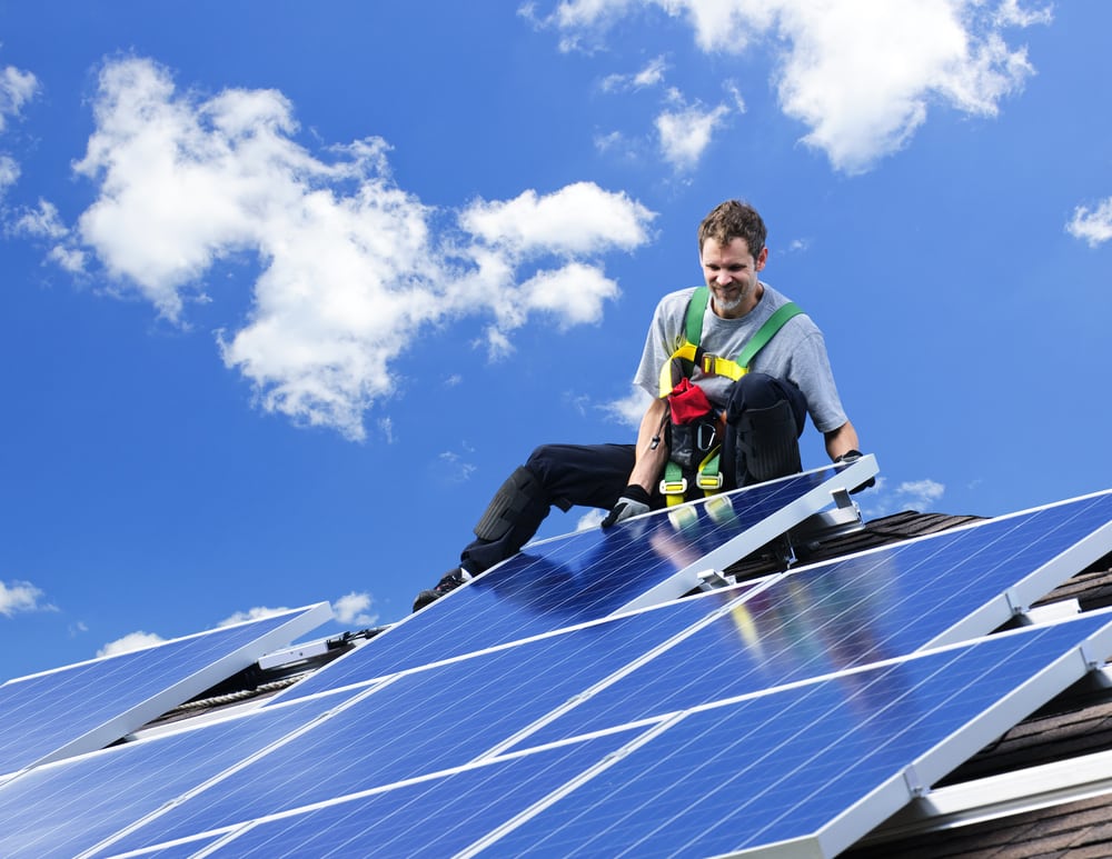 Male worker in harness performing solar panel installation in Los Angeles on roof