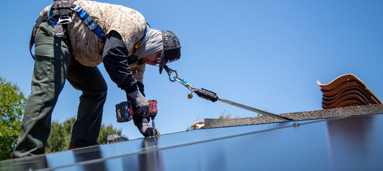 Installer bolting solar panel to a roof surrounded by new tiles.