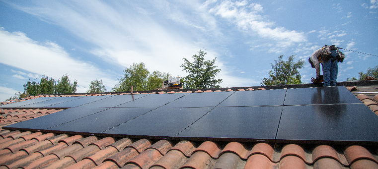 Installer finishing solar panel installation on clay tile roof.