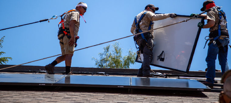 Three installers moving solar panel into place on an asphalt shingle roof.