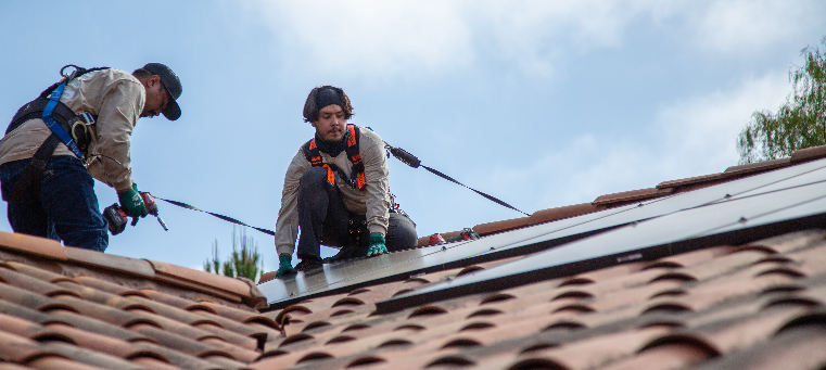 Two installers setting solar panel in place while holding a power drill.