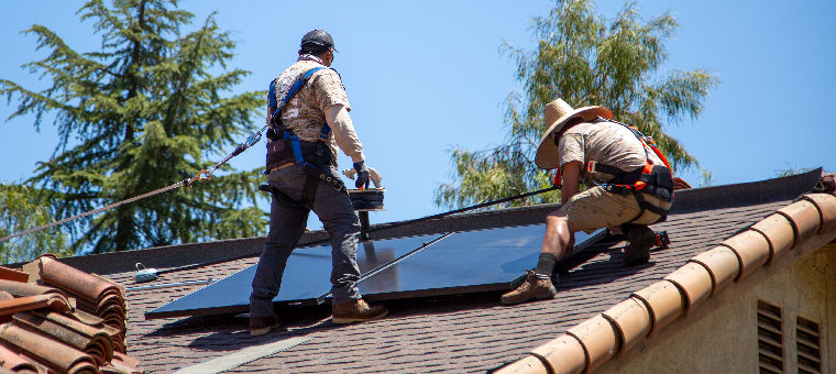 Two installers bolting solar panel to shingle roof.