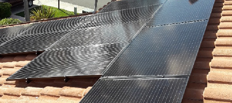 Eleven solar panels on clay-tile roof of two-story home.