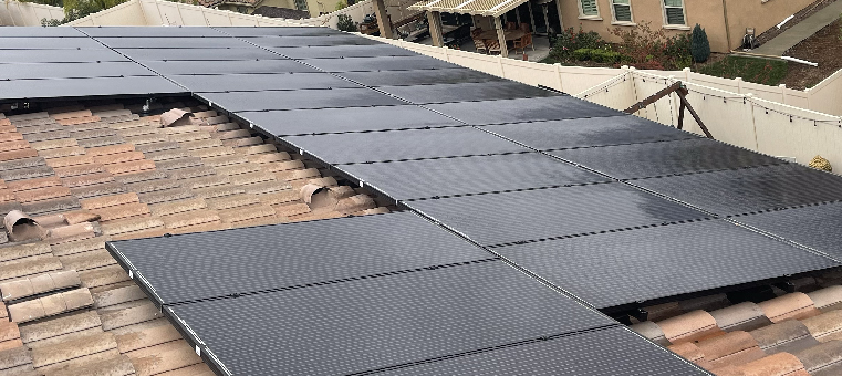 Thirty solar panels on a clay-tile roof on an overcast day.