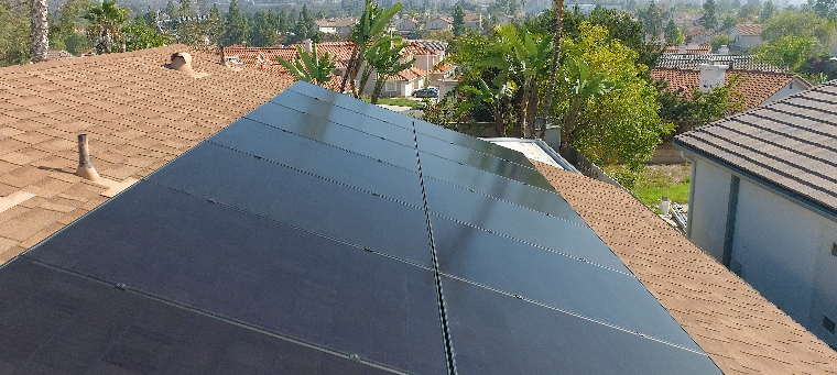 Thirteen solar panels on asphalt shingle roof surrounded by trees.