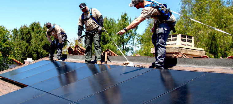 Three solar panel installers on roof of single family home.