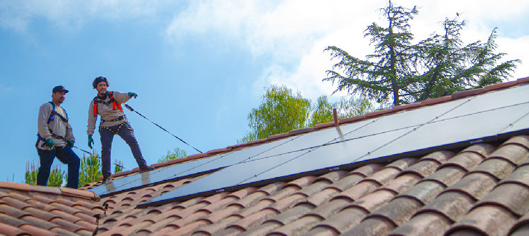 Two solar panel installers on clay tile roof of single family home.