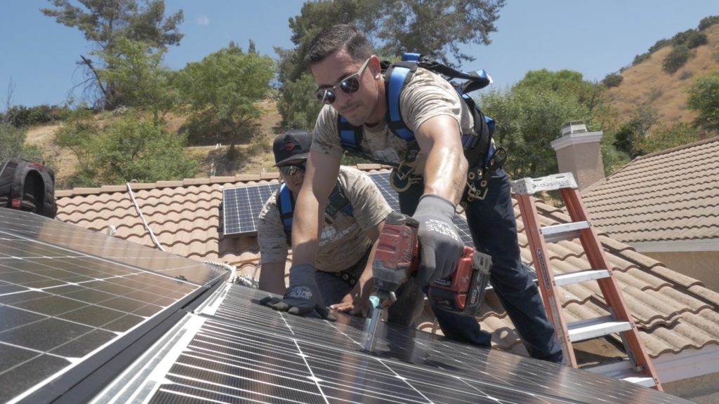 Two solar panel installers in Sacramento bolting a solar panel in place.