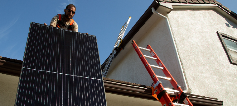 installer-lifting-solar-panel-onto-roof-ladder