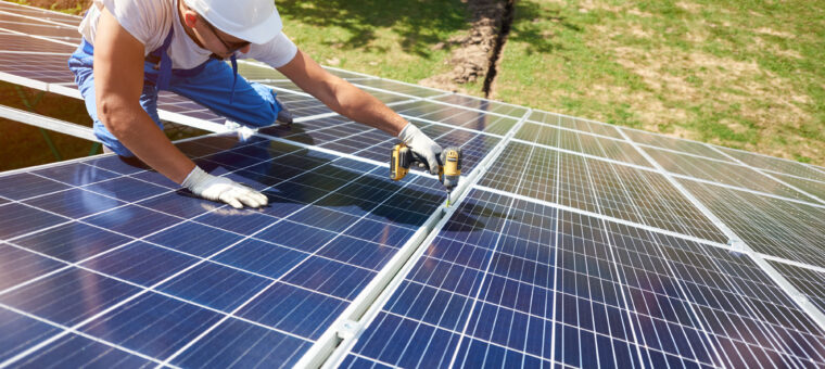 Professional worker installing solar panels on the green metal construction