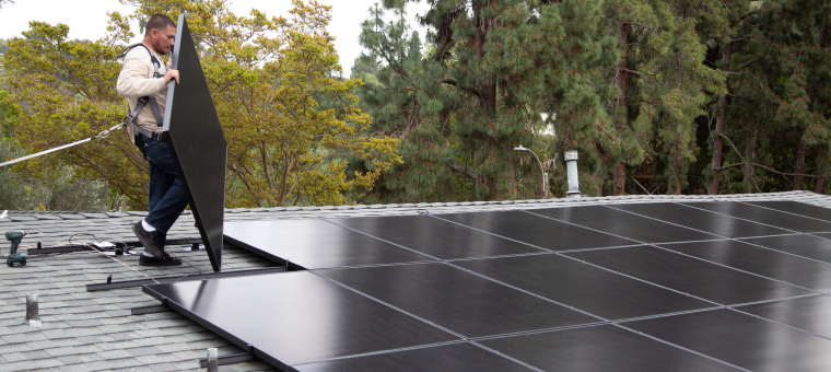 Solar installation specialist carrying solar panel on roof.